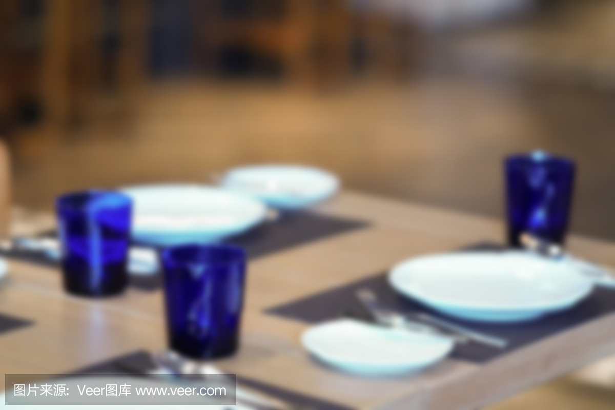 盘子,勺子,叉子和蓝色的玻璃在木桌上,模糊
